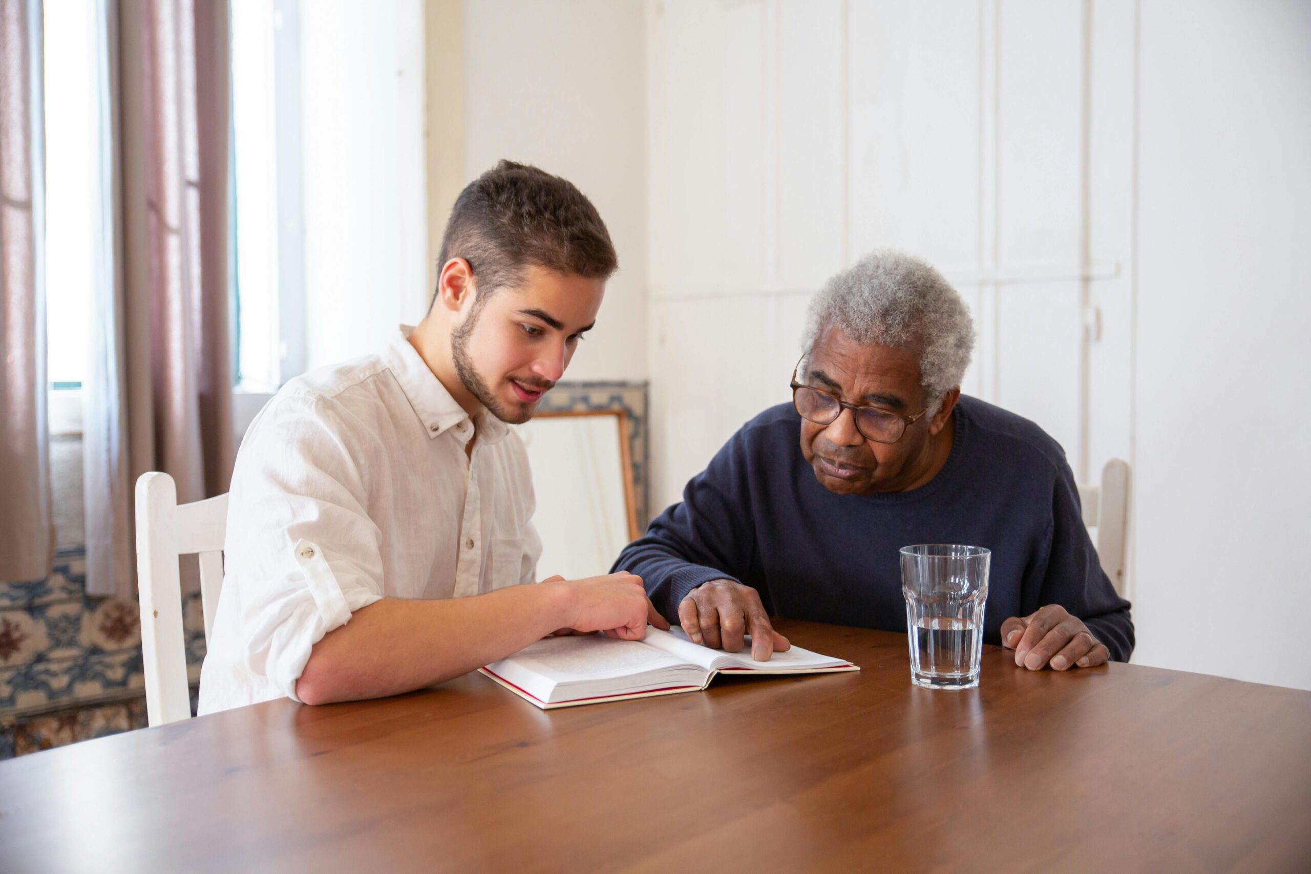 young man assisting a senior man reading a book as part of in-home senior care